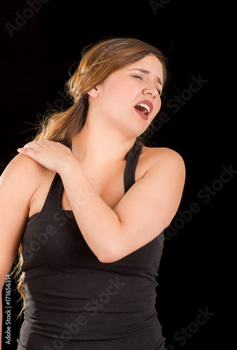 Beautiful young woman suffer from shoulder pain in a black background © Fotos 593