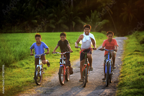Bild auf Leinwand Four young boys happily riding bicycles on a rural path at 5:30 PM during golden hour