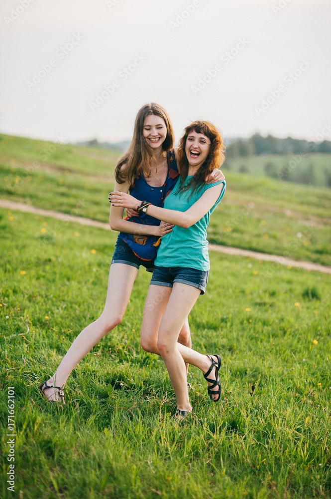 Two young lovely girls with long hair and naked legs spending time at  nature outdoor. Women friendship. Weekend with beloved friend. Expressive  emotion. Laughing and smiling teenagers. Youth lifestyle Stock Photo