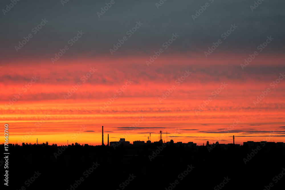Red bright sunset over the city. City industrial landscape against the backdrop of the setting sun. Sunset with silhouette of city buildings and factory pipes