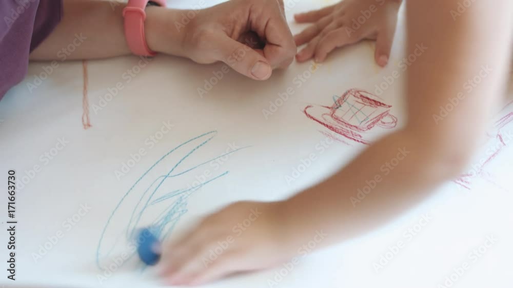 Little kid draws a scribble in blue on white paper. The view from the top.