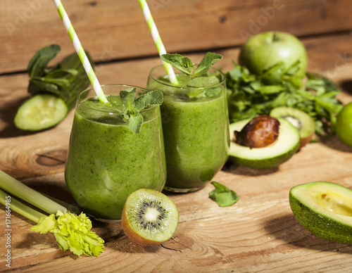 Freshly blended green smoothie in glasses with straws. Wooden background.