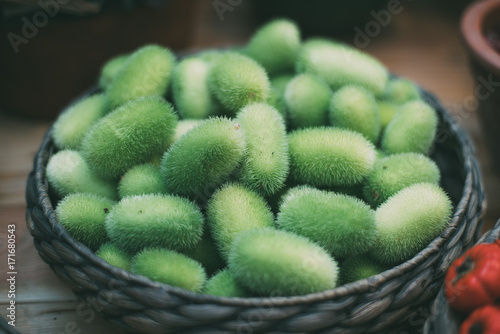 Braided basket staying on wooden table full of green and hairy tropical vegetable cucumis dipsaceus (also called Wild Cucumber or Hedgehog Gourd, or Teasel Gourd) recently gathered photo
