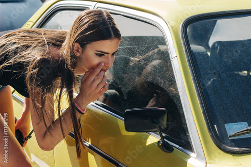 Young female model looking her self at rearview mirror of yellow oldtimer photo