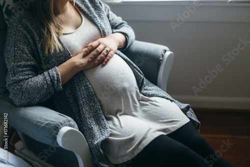 Full Term Pregnant Mother Sitting in Rocking Chair Patiently Waiting For Baby To Arrive photo