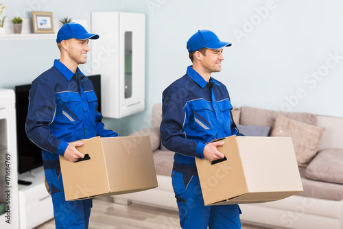Two Delivery Man Carrying Cardboard Box In New Home © Andrey Popov