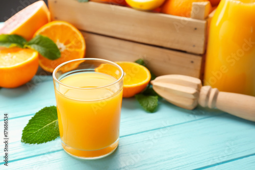 Glass of fresh juice and oranges in box on wooden table