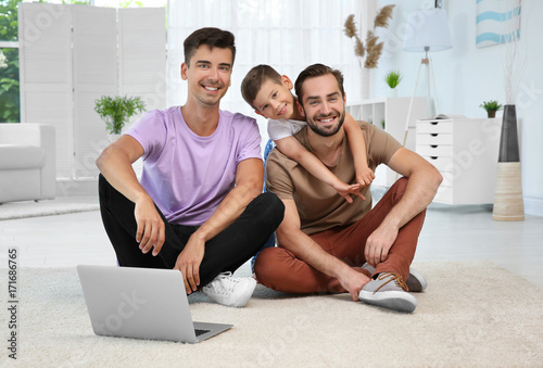 Male gay couple with foster son sitting on floor at home. Adoption concept