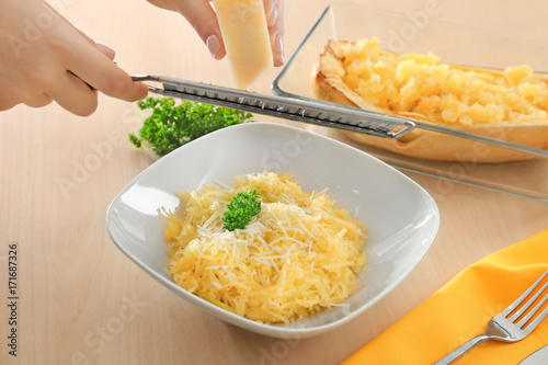 Woman grating cheese on spaghetti squash in plate photo