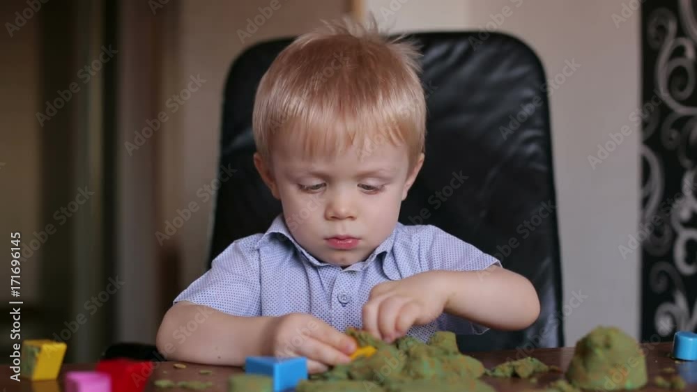 Happy smiling child plays kinetic sand at home. Little boy three years playing with kinetic sand at home, close-up.