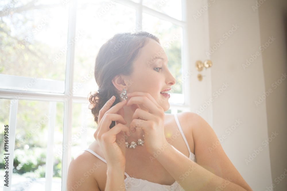 Beautiful bride wearing earring while standing by window Beautiful bride wearing earring while standing by window