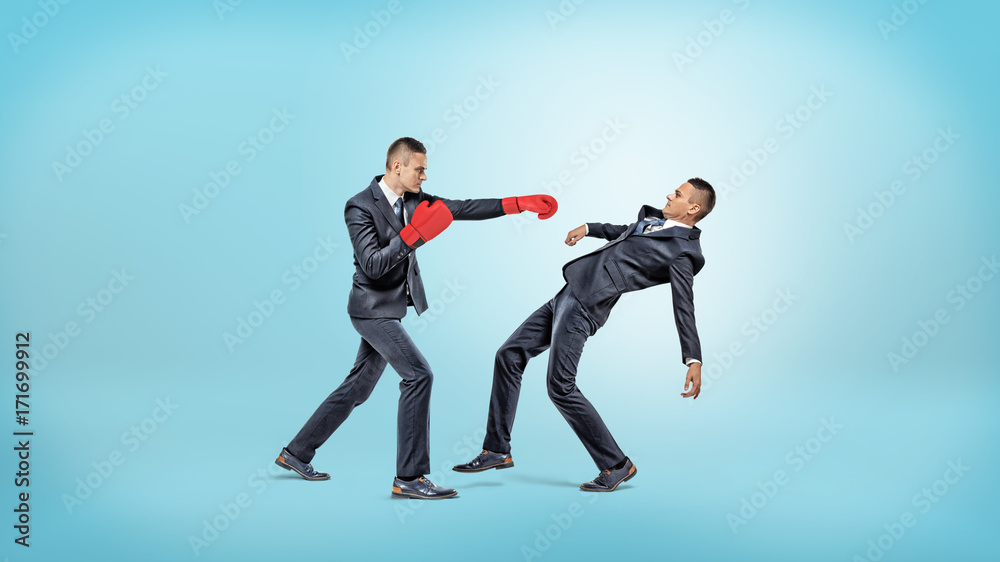 A businessman in boxing gloves fails to punch another man who manages to avoid the kick. A businessman in boxing gloves fails to punch another man who manages to avoid the kick.