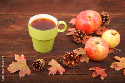 Autumn concept, fallen red-yellow leaves with apples, pine cones and a cup of tea on a wooden table. Thanksgiving Day.