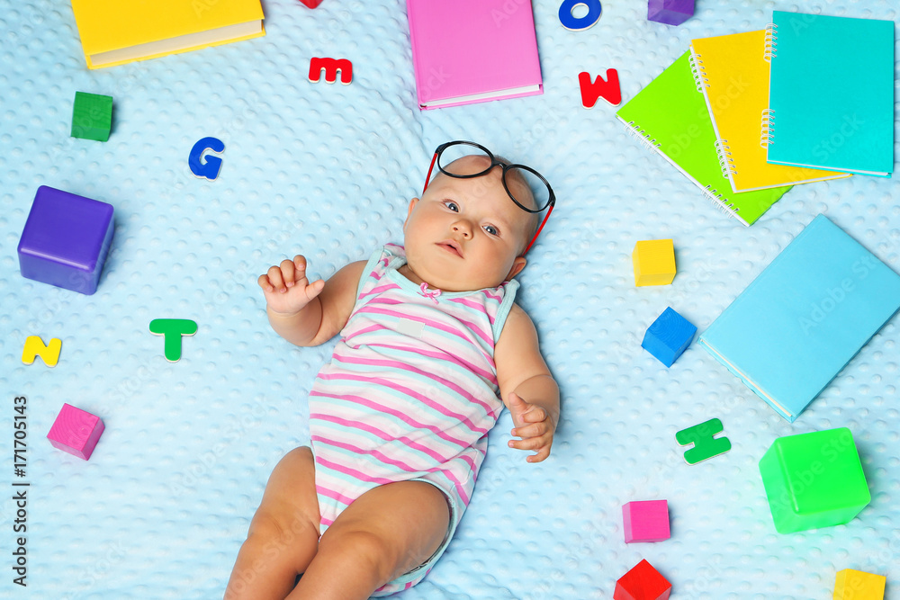 Little newborn baby with books and letters on bed