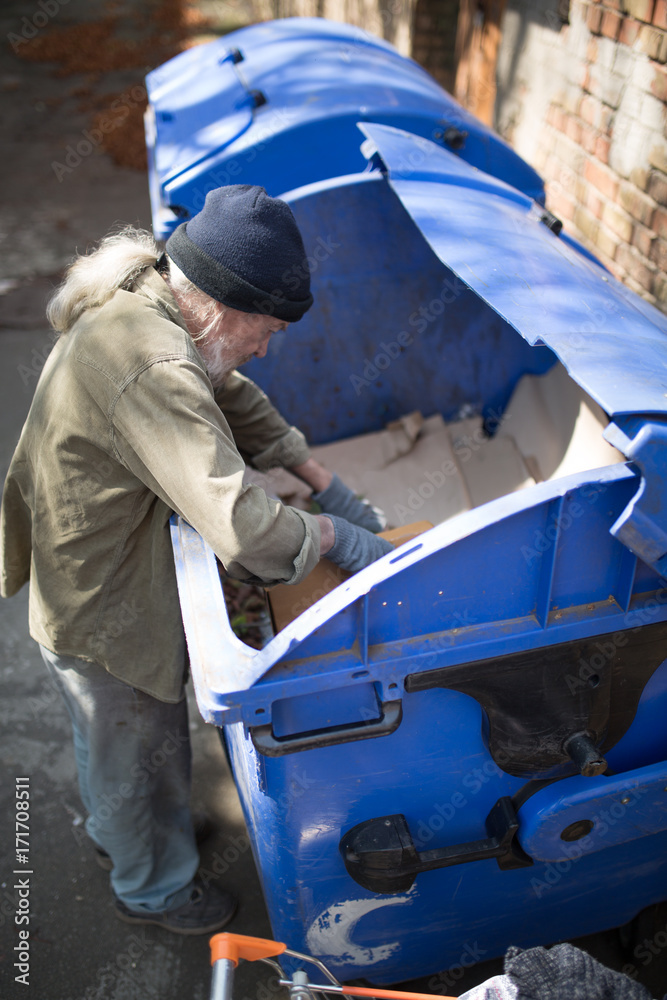 Top view of old homeless male digging in thrash can. Tramp searching for food and empty bottles.