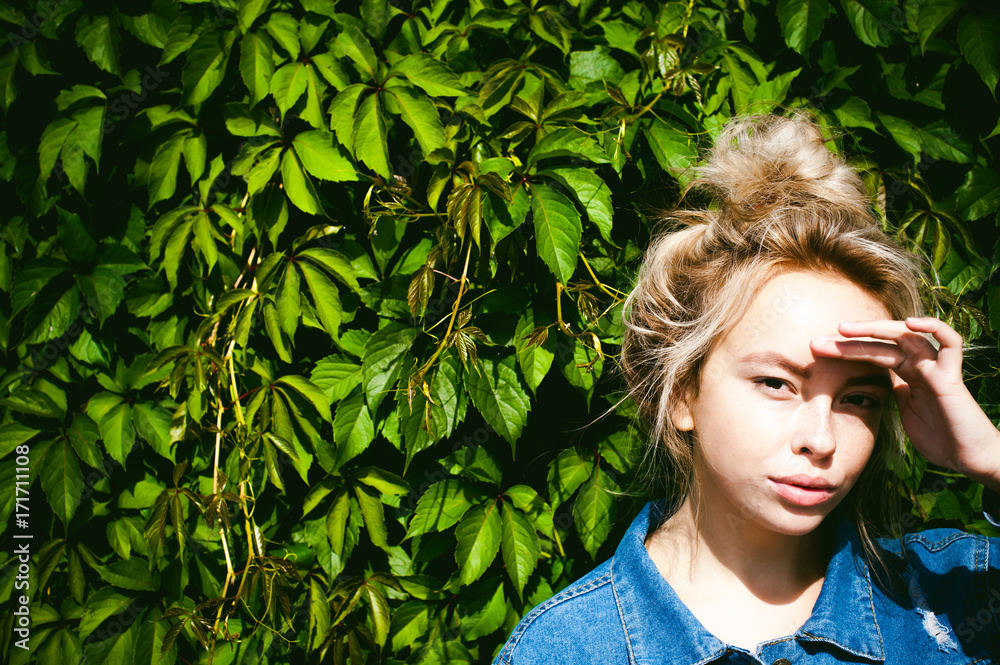 young beautiful woman in jeans clothes outdoors. portrait of a girl with freckles on her face, stylish girl against background of green leaves of a climbing plant, on a sunny summer autumn day. young beautiful woman in jeans clothes outdoors. portrait of a girl with freckles on her face, stylish girl against background of green leaves of a climbing plant, on a sunny summer autumn day.