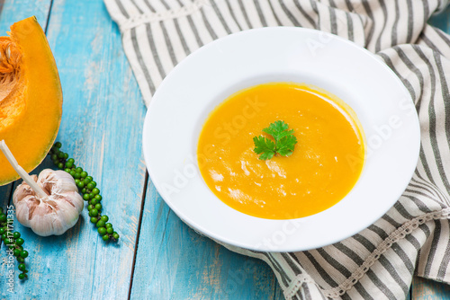 Pumpkin and carrot soup with cream and parsley on blue  wooden background.