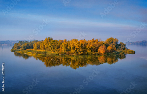 Island with yellow deciduous forest on a wide river. © olegphotor
