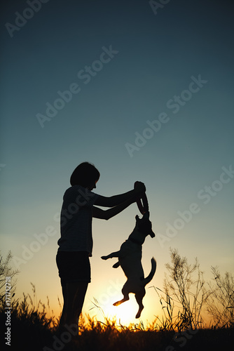 Silhouette of woman playing with dog at sunset.