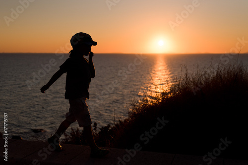 Boy walk during the sunset with sea on background photo