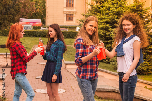 The young happy women students standing outdoors and smiling and keeping the bottles of juice