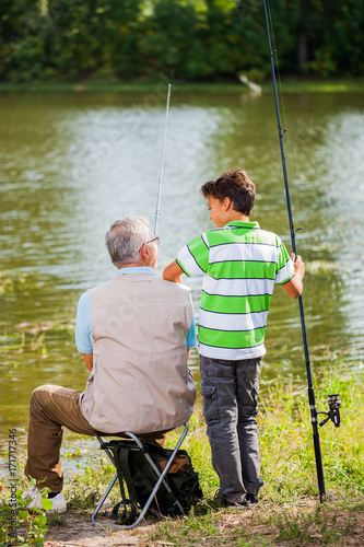 Grandfather and grandson are fishing on sunny day.
