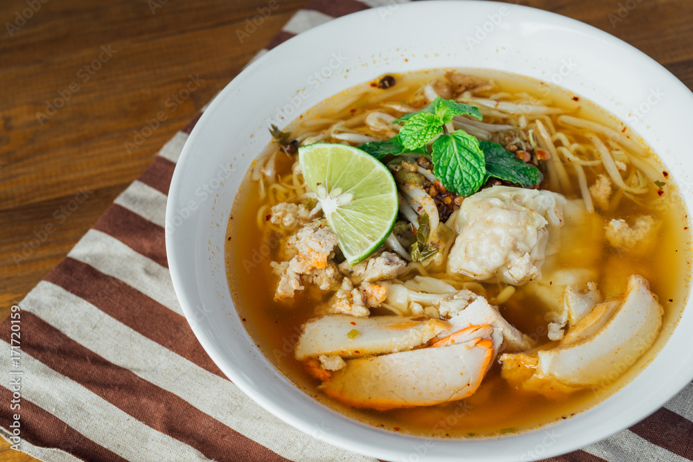 Noodle pork soup with Tom Yam spicy in white bowl on wooden table background. Noodle pork soup with Tom Yam spicy in white bowl on wooden table background.