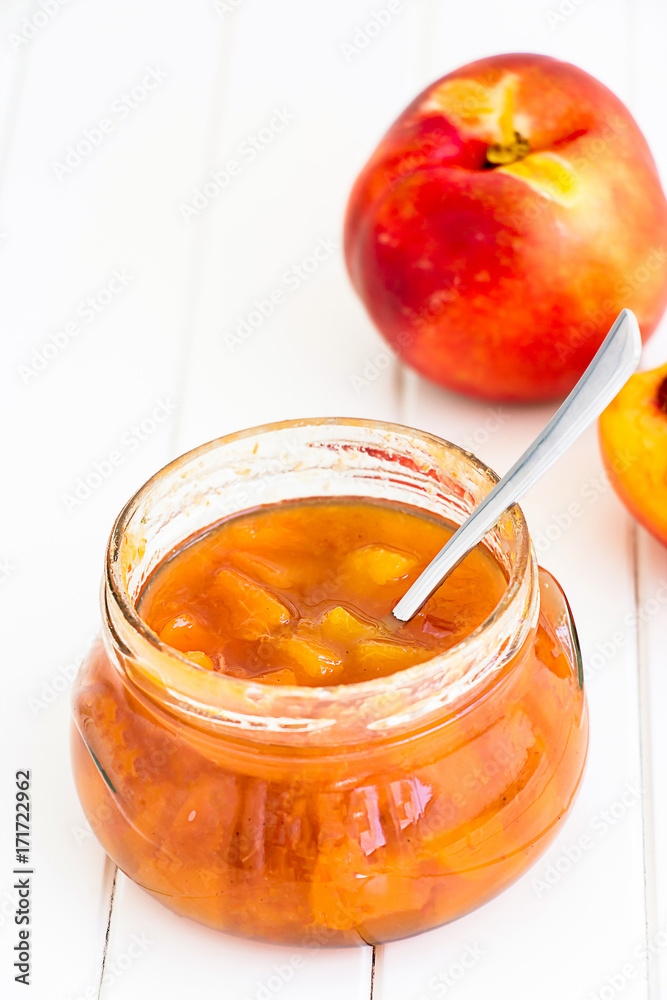 Nectarine (Peach, Apricot) jam confiture in glass jar and spoon on white wooden background. Vertical. Selective focus. Copy space for your text.