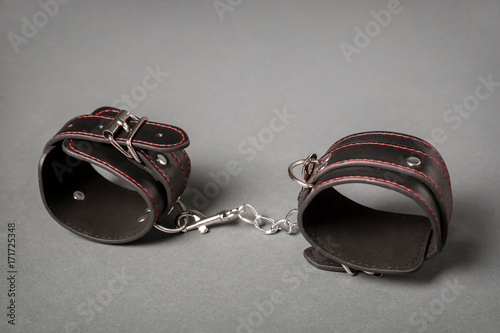Black leather handcuffs on gray background. Sex toy.