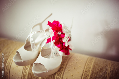 Bride's white shoes with garter stand on the sofa