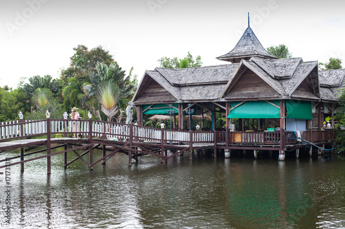 Thai picturesque tropical landscape with wooden buildings and lake with a bridge and palms © Shaganart