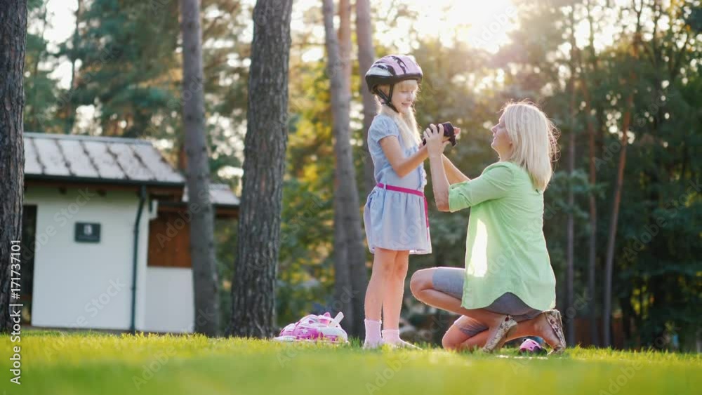 Happy time together. Mom puts on protective mittens to daughter, they prepare to skate on roller skates Happy time together. Mom puts on protective mittens to daughter, they prepare to skate on roller skates