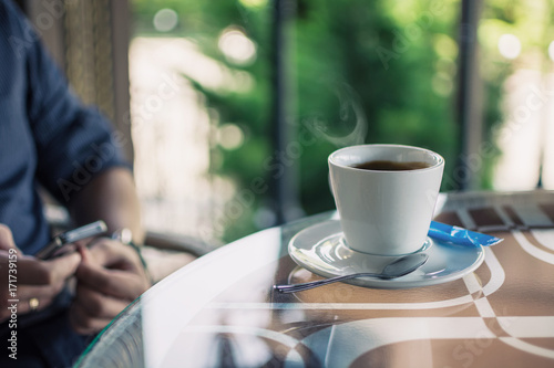 cup of coffee on a table in a cafe and men s hands with a phone in a blurry background