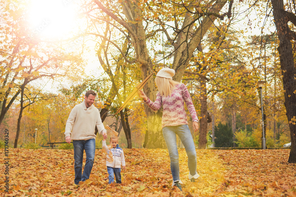Mother and father playing with son in park at autumn/ flying kite