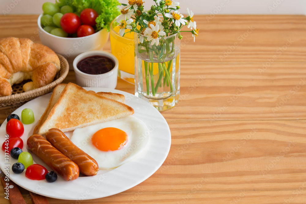 Homemade breakfast with sunny side up fried egg toast sausage fruits vegetable strawberry jam and orange juice in top view. Delicious homemade american breakfast concept for background or wallpaper. Homemade breakfast with sunny side up fried egg toast sausage fruits vegetable strawberry jam and orange juice in top view. Delicious homemade american breakfast concept for background or wallpaper.