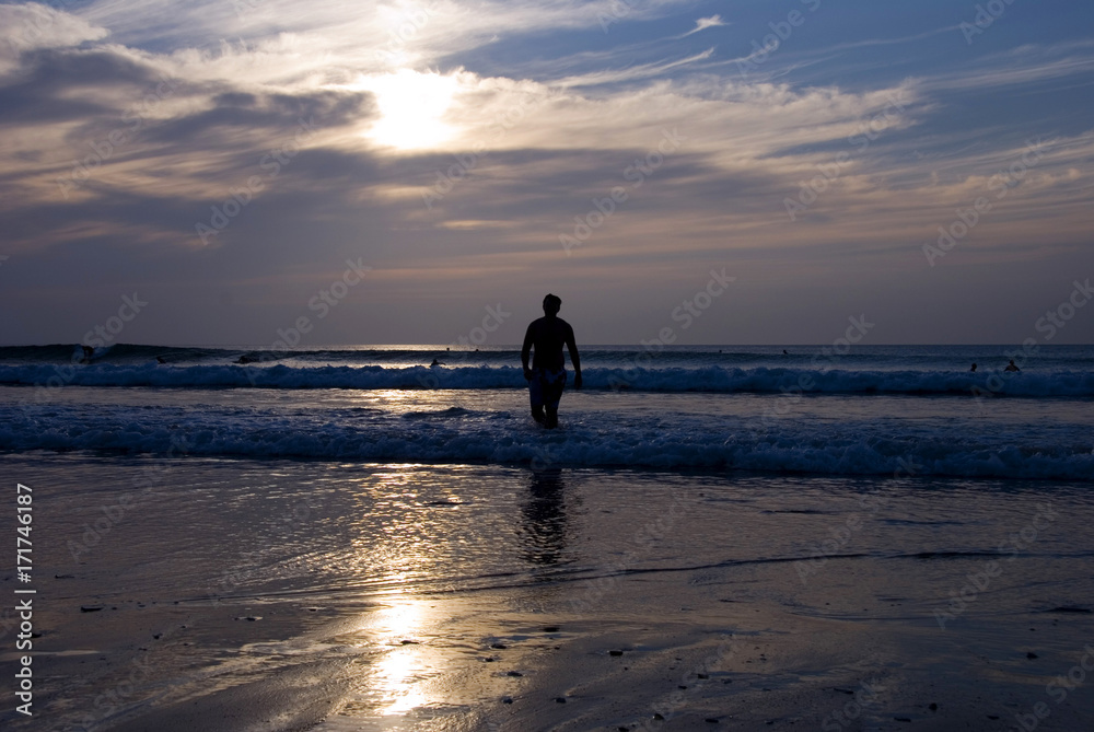 Silhouette of Night Surfer walking along the beach as sunset