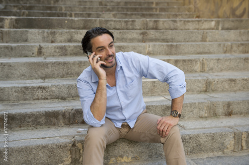 attractive latin man on city staircase talking happy on mobile phone looking satisfied and confident photo