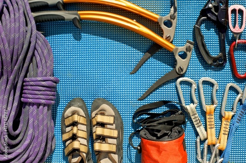 Climbing equipment laid out on a blue mat. Rope, ice tools, ascender, belay/rappel device with carabiner, quickdraws, chalk bag, climbing shoes.  photo