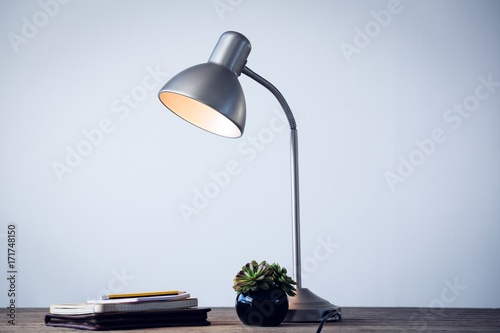 Принти на полотні Illuminated desk lamp by books on table