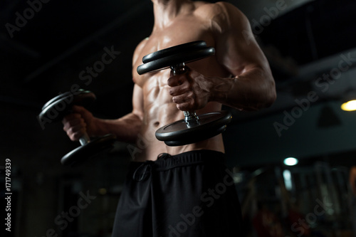 Платно close up of man with dumbbells exercising in gym