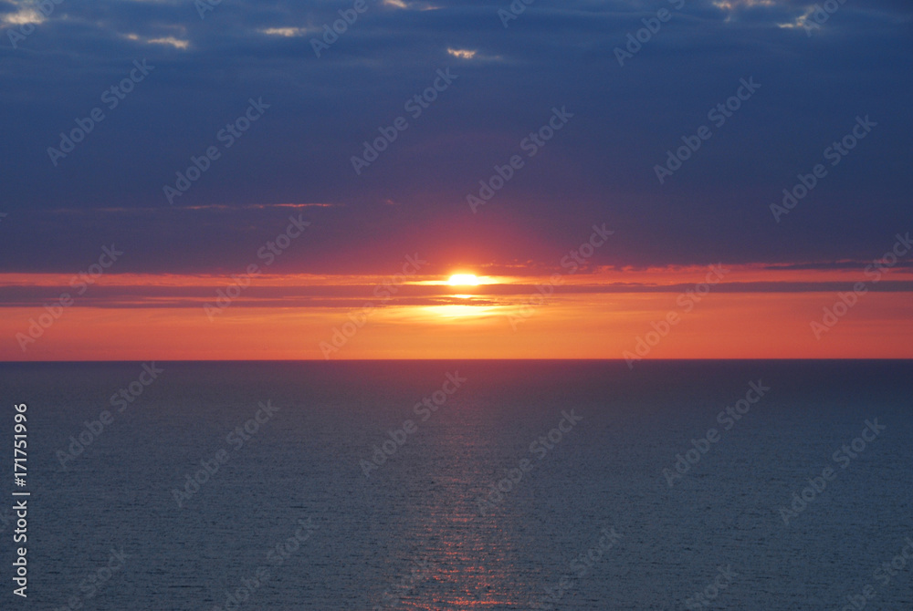 Beautiful Red and Blue Sunset or Sunrise horizon over the Ocean, sun peering through the cloudy sky