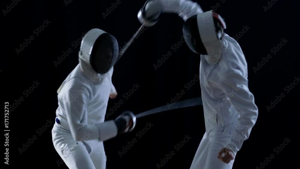 Two Professional Fully Equipped Fencers Expertly Fight with Foils. They Attack, Defend, Leap and Thrust and Lunge. Shot in Slow Motion and on Isolated Black Background. 