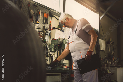 Senior man in workshop. Man holding his book planner and searching tool.