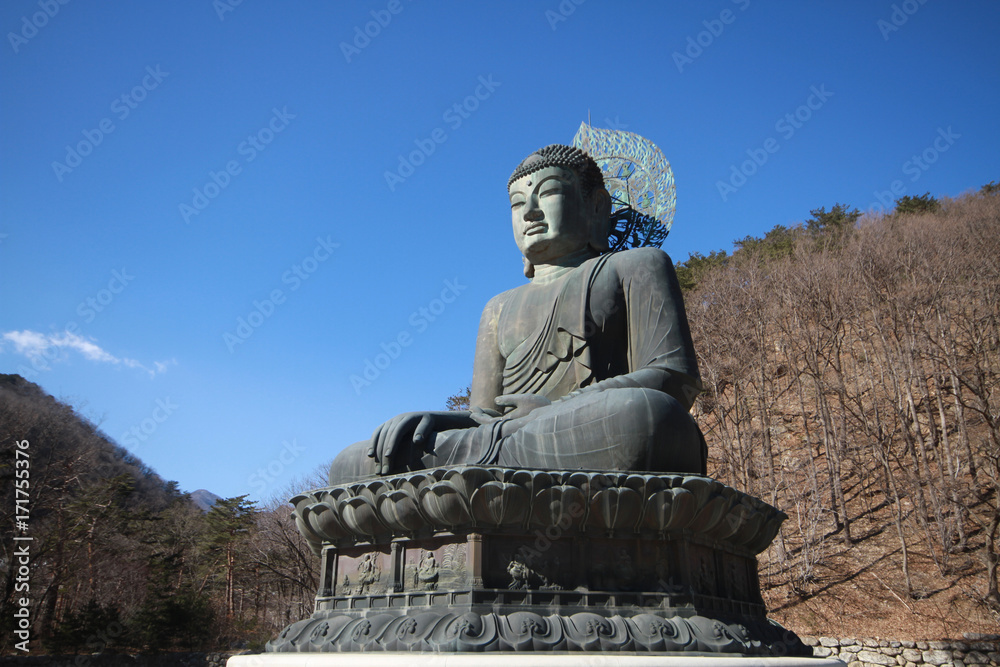A ancient metal carving of sitting peace buddha in front of tree mountain and painted with green color at large historical temple at south korea A ancient metal carving of sitting peace buddha in front of tree mountain and painted with green color at large historical temple at south korea