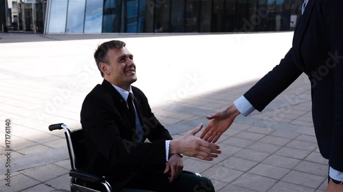 Young attractive businesswoman in formal suit shaking hands with disabled employee outdoor nead cool modern business centre building at sunrise. Super slow motion. Middle shot. 240 fps. photo