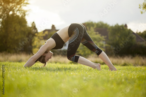 Young brunette doing yoga stretching back in the park