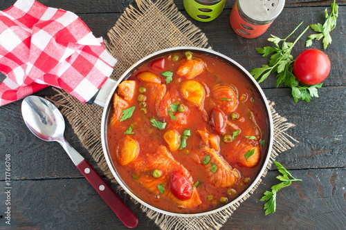 Fish fillet cooked in tomato sauce with green peas and cherry tomatoes on a plate on a wooden background. Healthy eaing concept. Easy cooking. photo