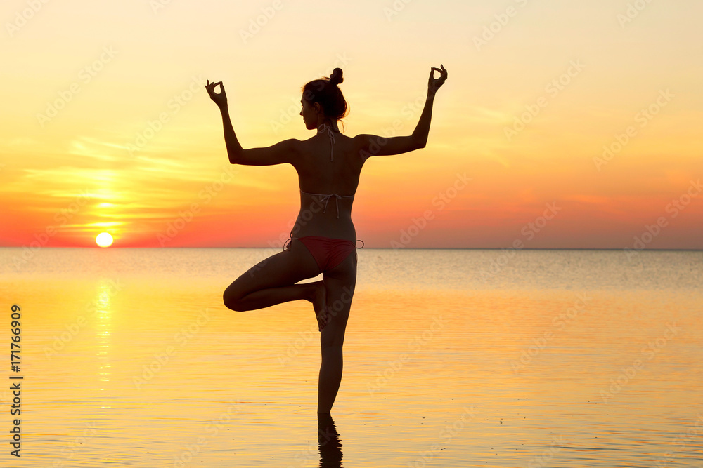 young beautiful brunette woman doing yoga at sunset on beach