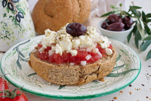 DDakos traditional Greek appetizer on a traditional plate with ceramic olive oil jar, dry rye bread, olives and olive branch. Healthy eating concept. Mediterranean lifestyle