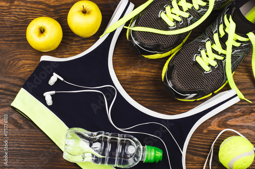 Sports items: sneakers, ball, bottle of water and headphones on the wooden background